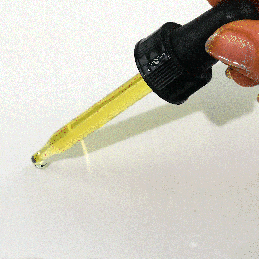 A glass dropper dispenses a single drop of golden liquid onto a white surface.