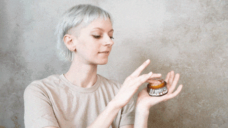 Woman holds a small jar of amber-colored styling balm in her open palm.