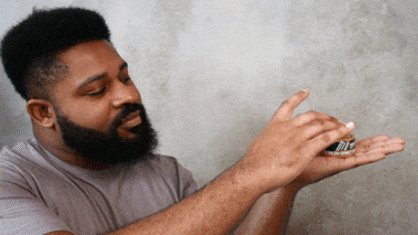 "Man holds a small, round container of beard balm in his hands, preparing to apply it."