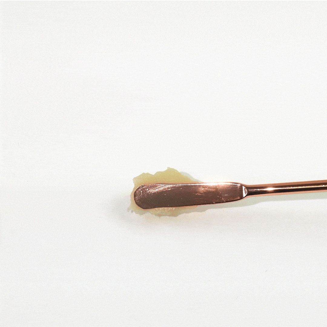 Rose gold dab tool scoops golden wax concentrate.