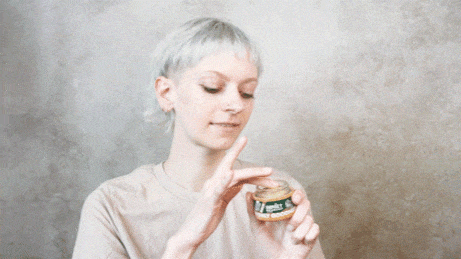 Woman opens a small jar of yellow moisturizer, preparing to apply it.
