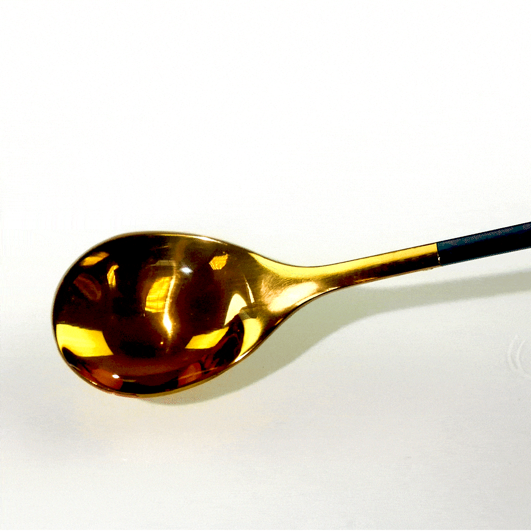 A shiny gold spoon with a matte black handle rests on a white surface.