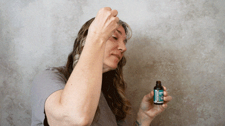 Woman applies liquid from a dropper bottle to her forehead.