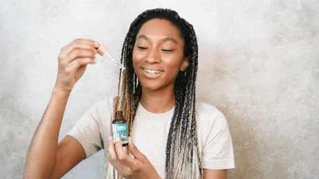 Woman smiles as she applies face serum from a dropper bottle.