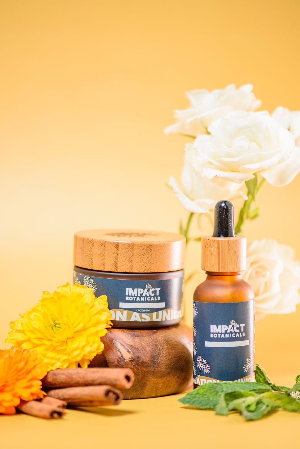 Impact Botanicals skincare products, including a moisturizer and serum, displayed with flowers, cinnamon sticks, and mint leaves on a yellow background.