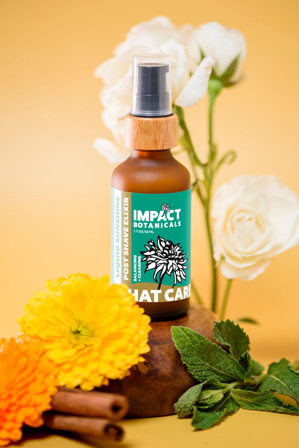 Amber bottle of Impact Botanicals Liquid Sunshine Post Shave Elixir surrounded by fresh flowers and herbs.