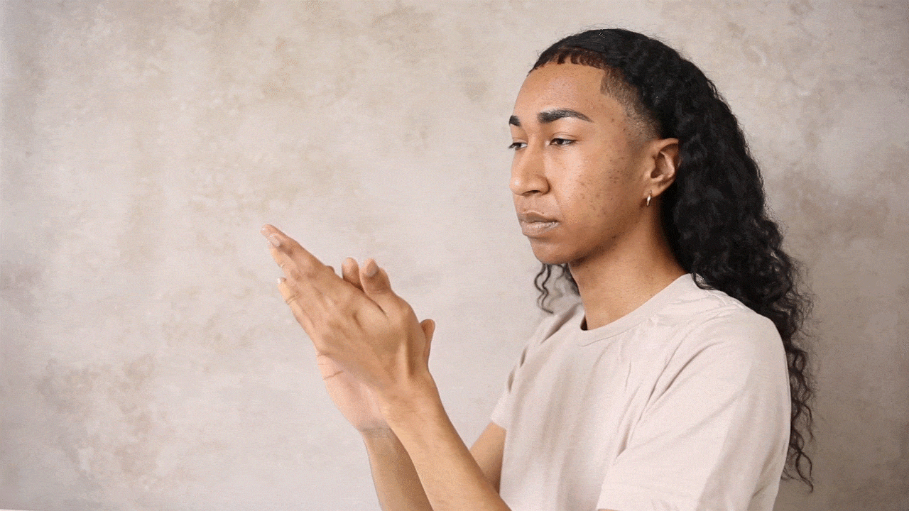 A person with long, dark, curly hair claps their hands together, showcasing a skincare or cleaning routine.
