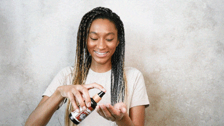 Woman smiles as she sprays hair oil into her hand.