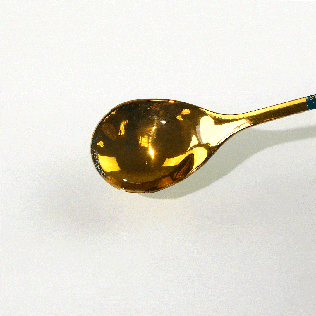 Shiny gold teaspoon reflects light on a white surface.