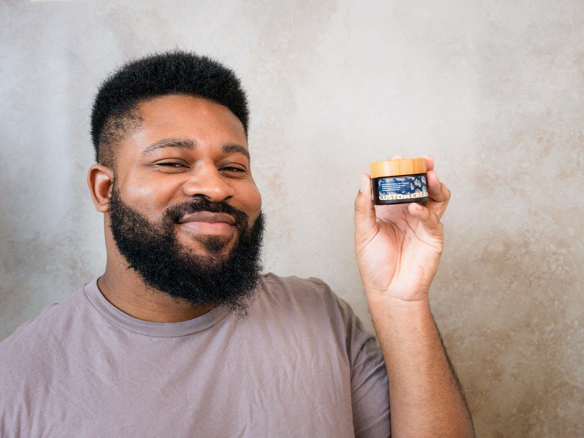 Man with short fade haircut and beard holds up a jar of custom-made hair cream.