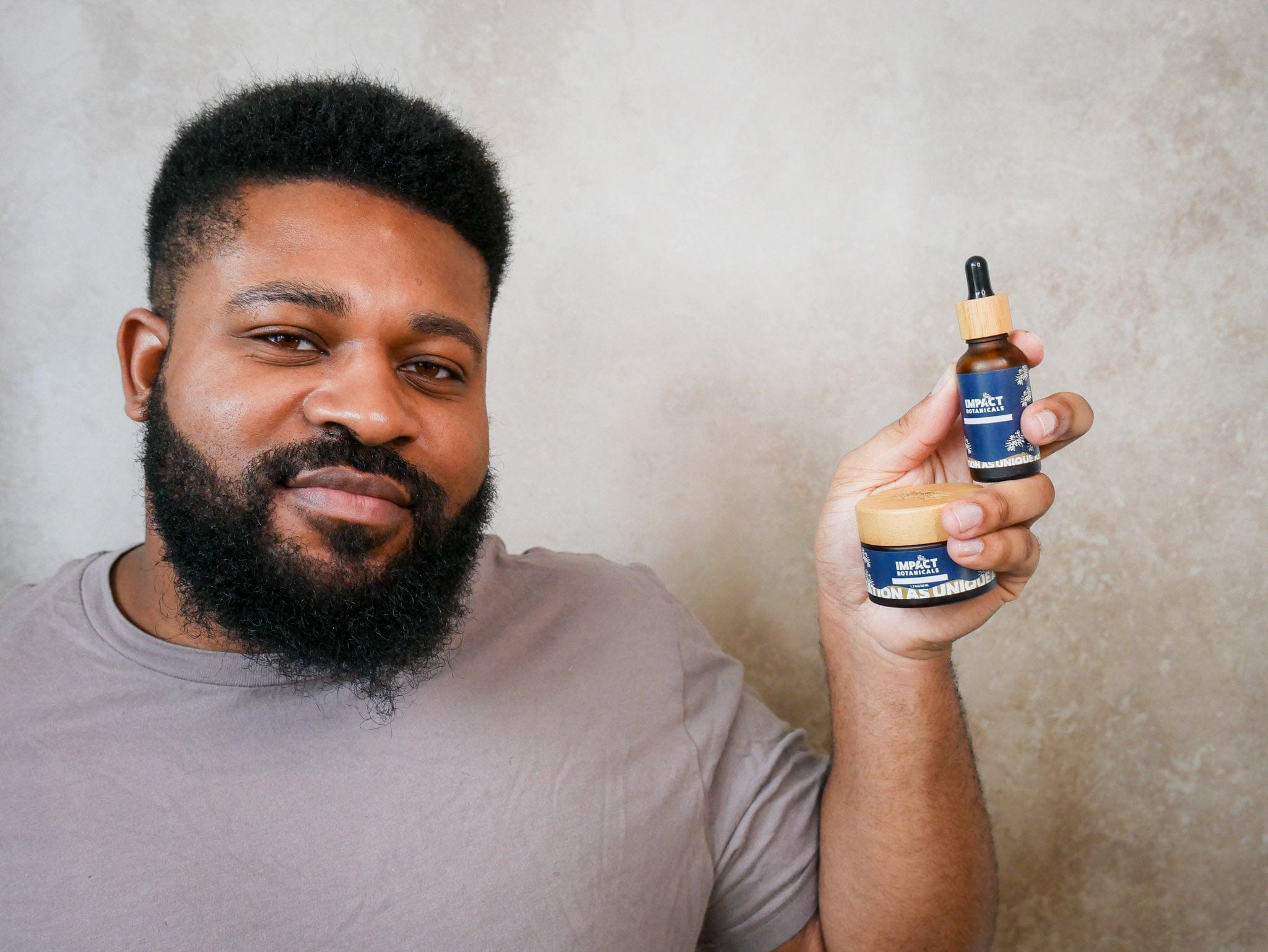 Man smiles while holding a bottle of beard oil and a jar of beard balm.