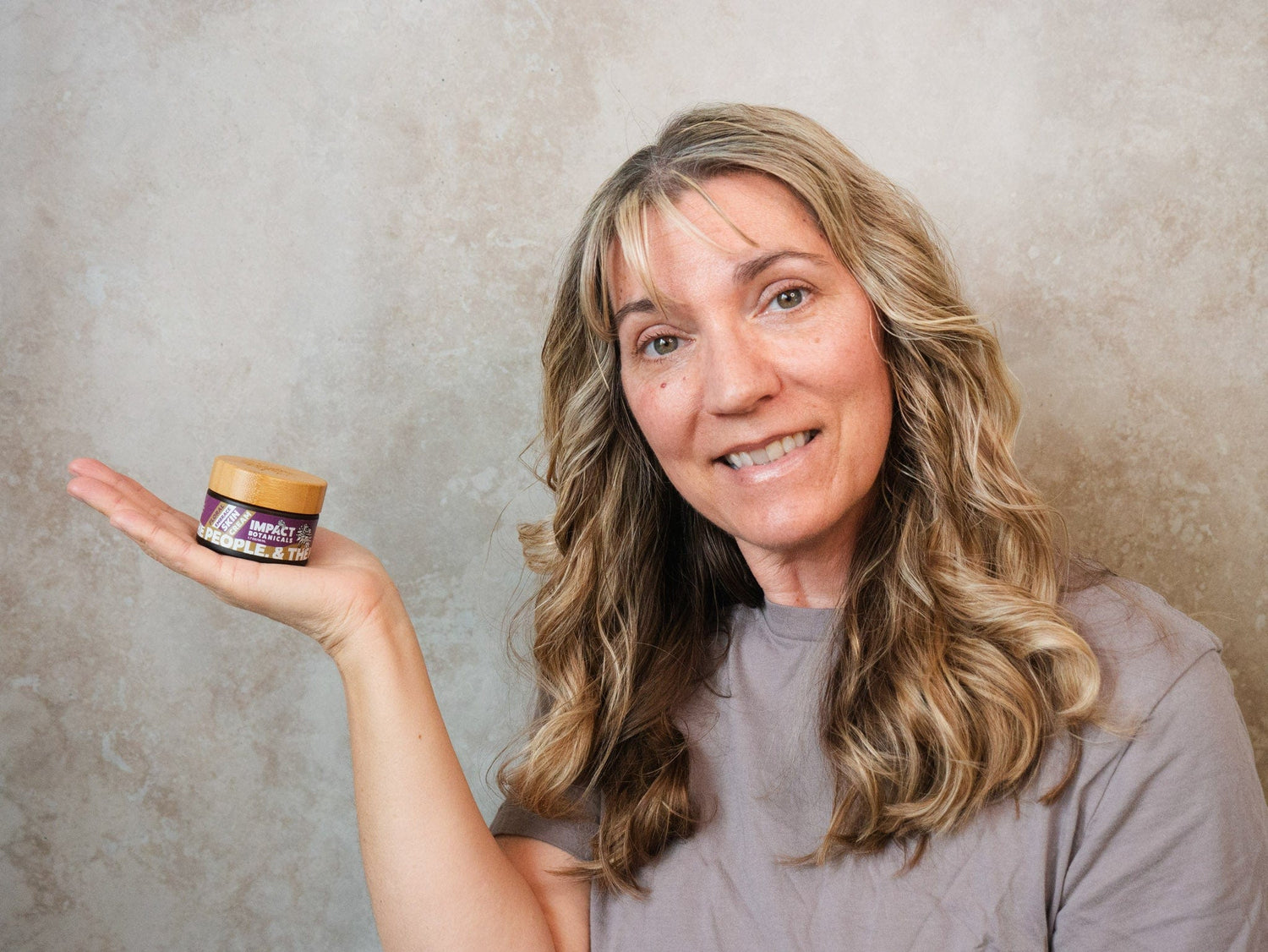 Woman smiles while holding out a jar of Impact Botanicals frankincense skin cream.