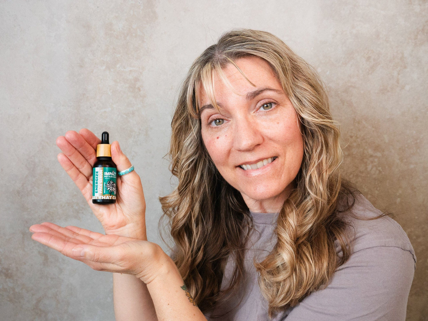 Woman smiles and holds a bottle of Impact Botanicals Energize Face Serum.