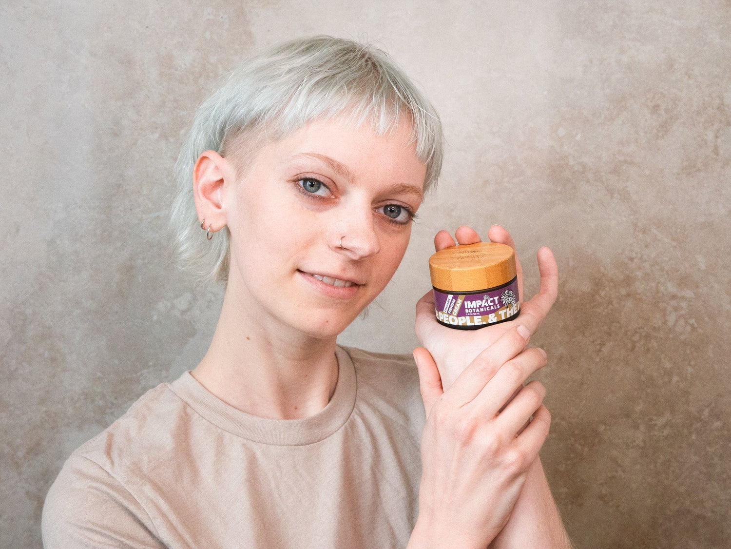 Woman holds a jar of "Impact Botanicals" calming cream.