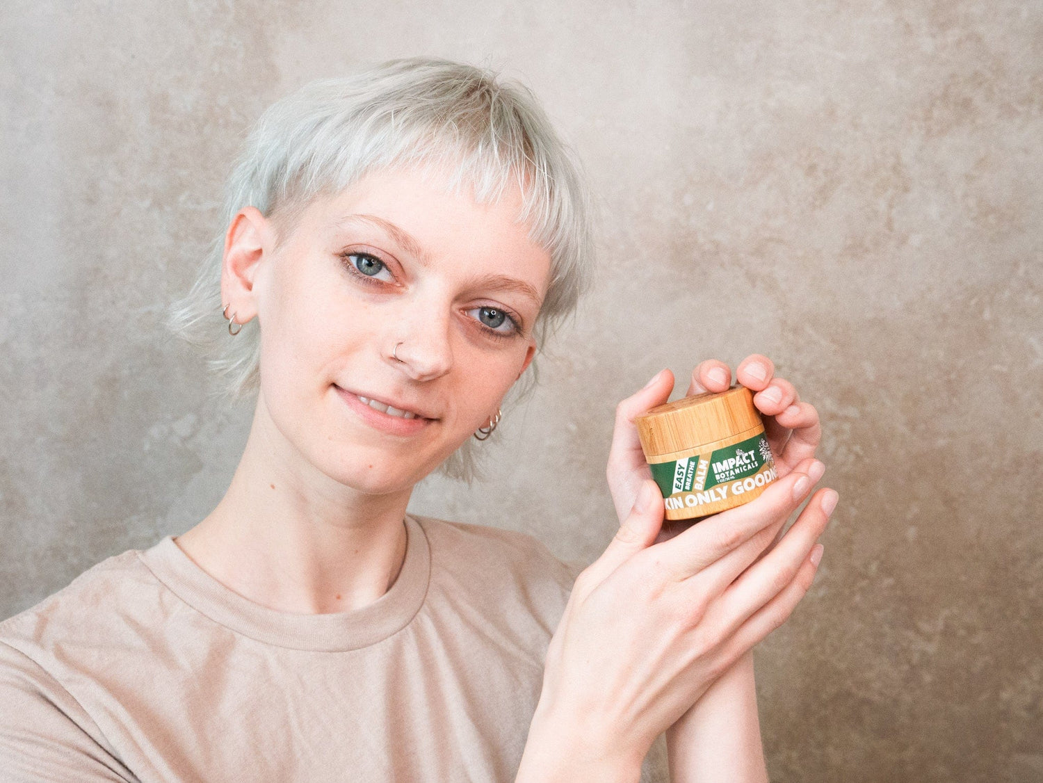 Woman holds a bamboo jar of "Easy Breathe" skin balm by Impact Botanicals.