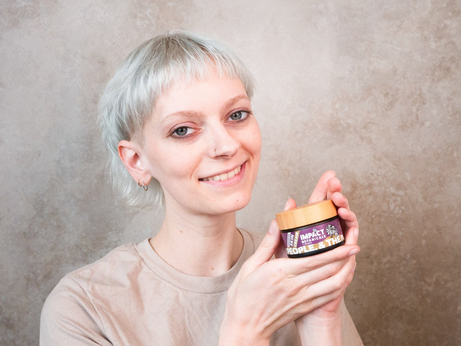 Smiling person holds a jar of "People & The Plants" Impact botanicals skin cream.