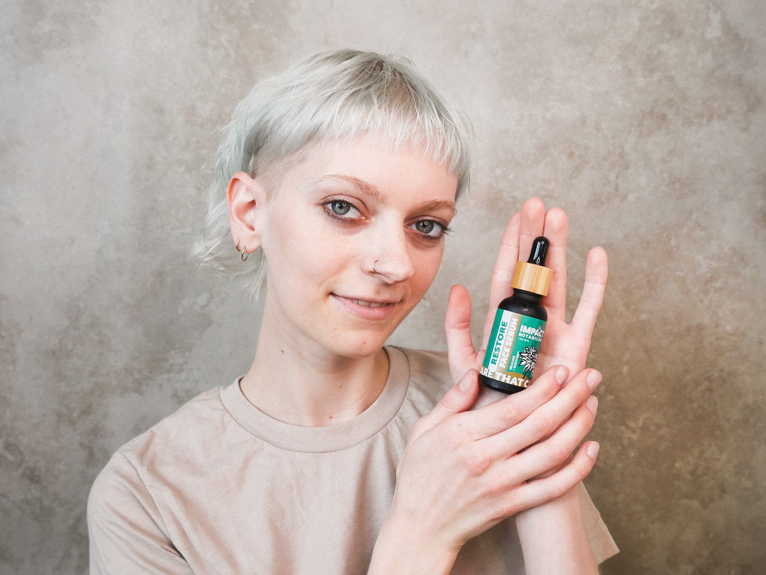 Woman holds a bottle of "Restore Face Serum" in front of a beige background.