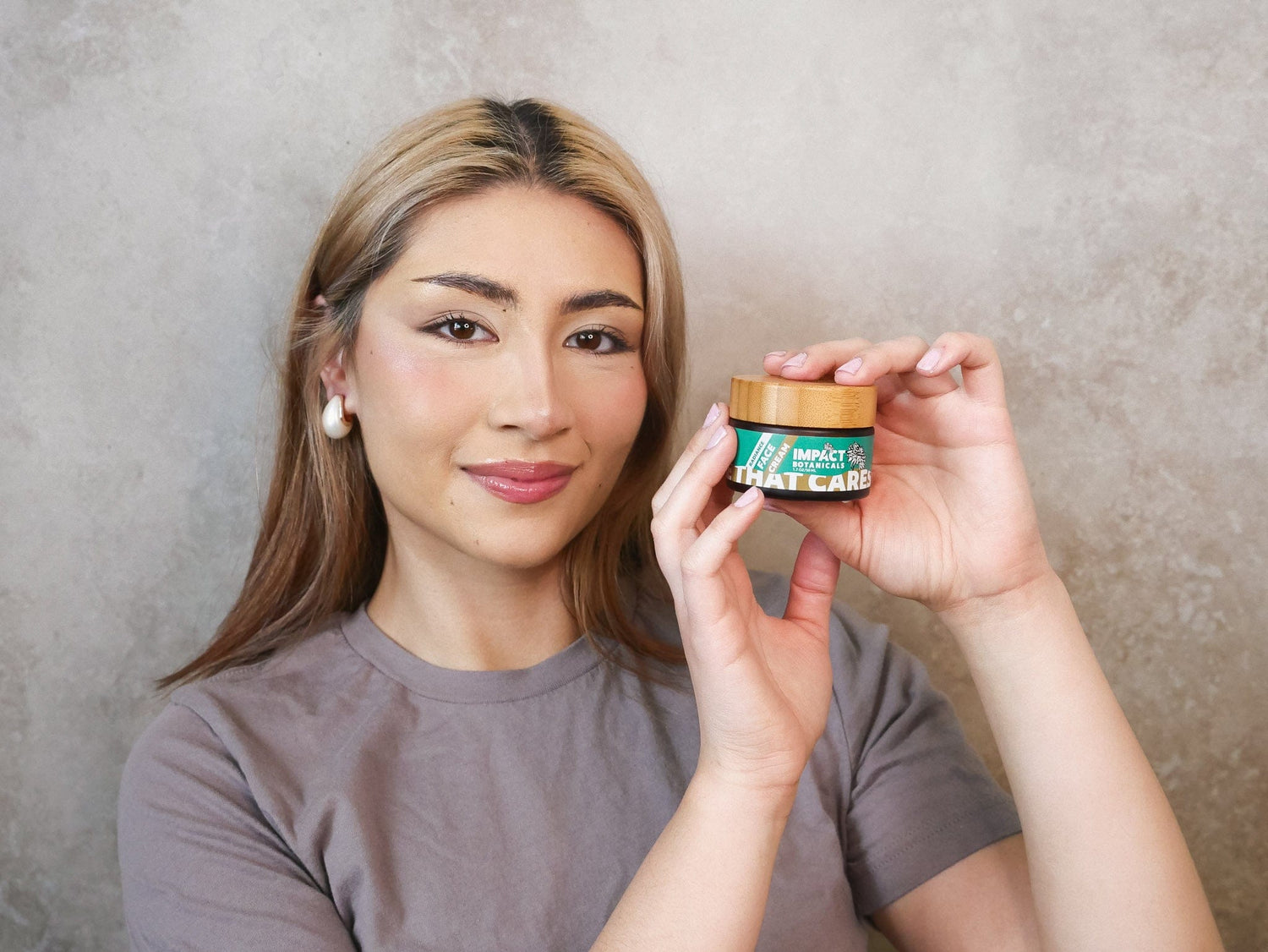 Woman holds a jar of Impact Botanicals face cream, showcasing the brand and product.