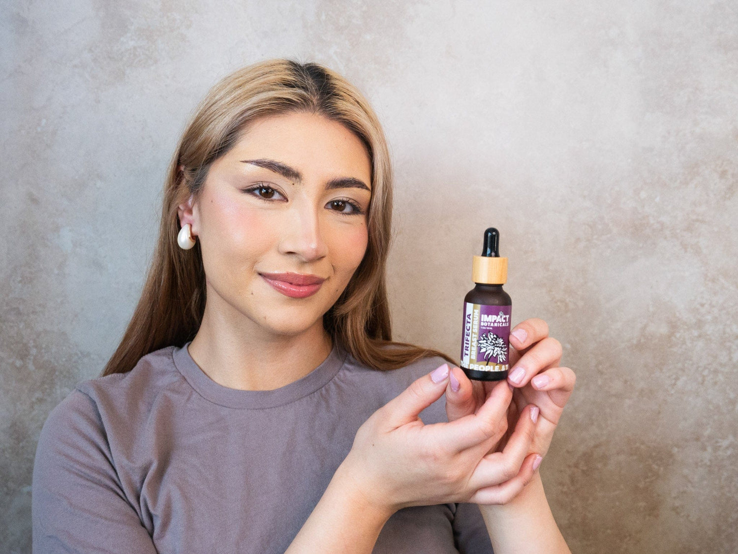 Woman holds a bottle of Trifecta Breast Serum by Impact Botanicals.