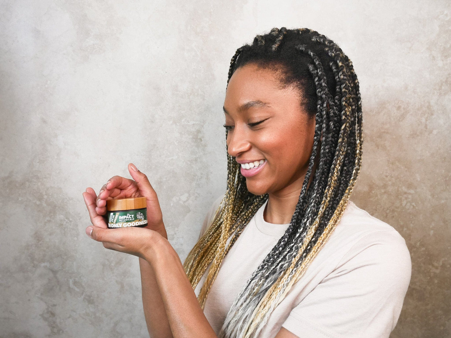 Woman with long braids smiles while holding a jar of "Only Goodness" face cream.