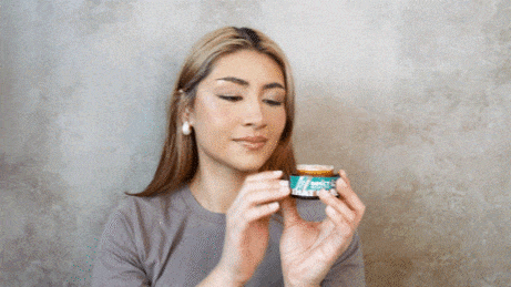 Woman holds a small jar of green moisturizer, examining it closely.