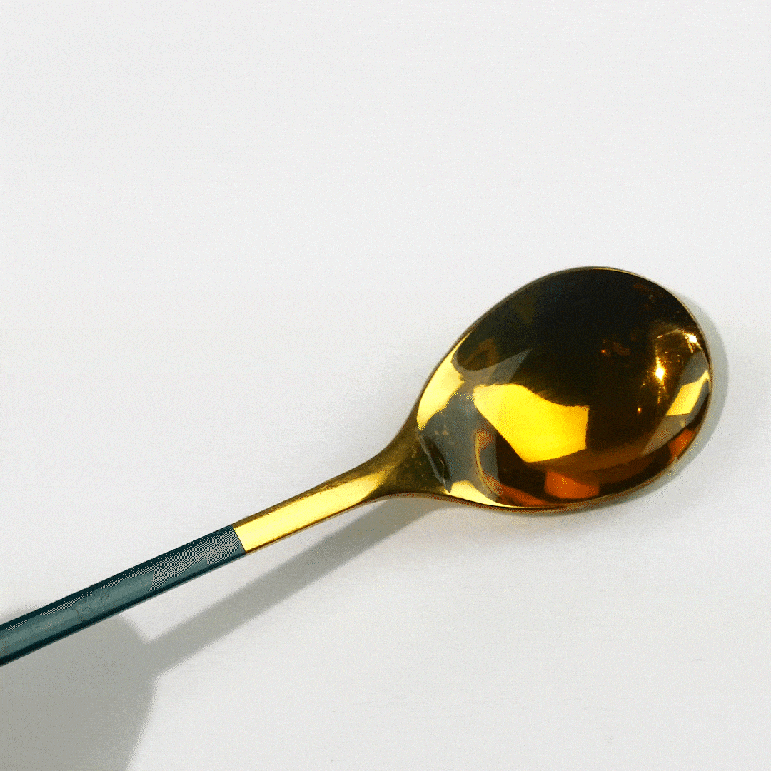 A gold spoon with a sleek, navy blue handle rests on a white surface, reflecting light from its polished bowl.