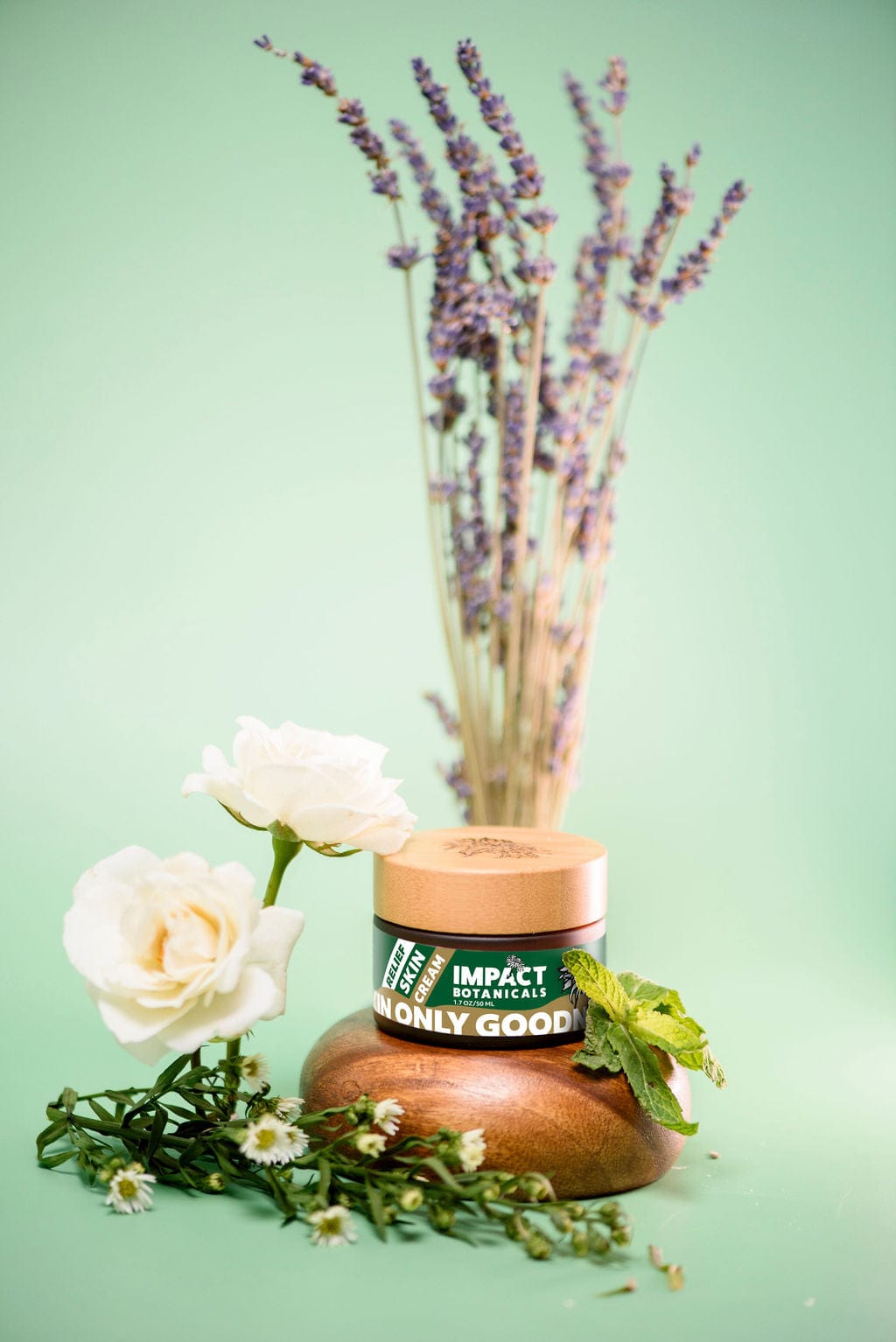 Impact Botanicals Relief Skin Cream Jar Surrounded by Fresh Flowers and Mint