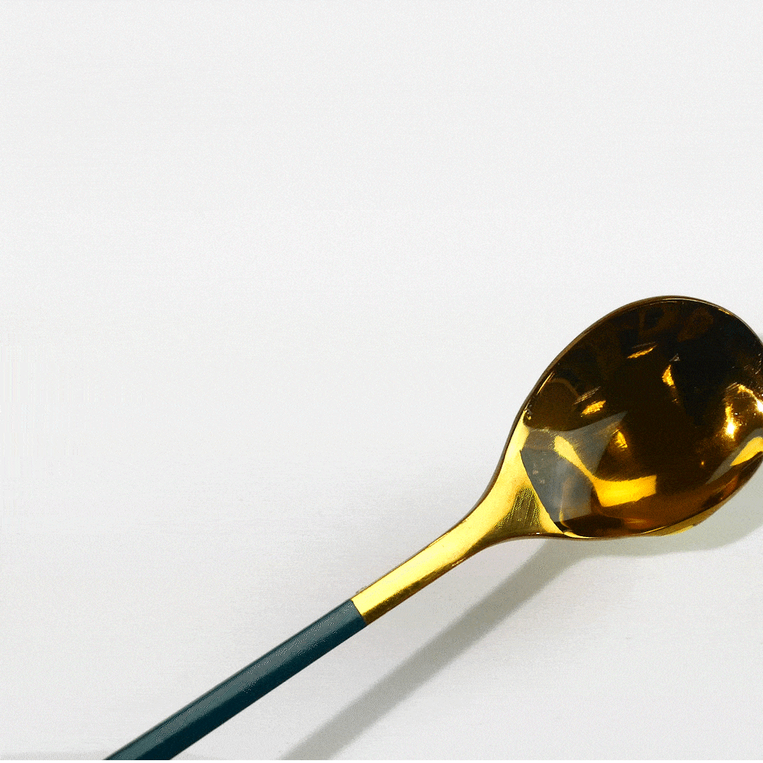 A gold spoon with a dark teal handle rests on a white surface.