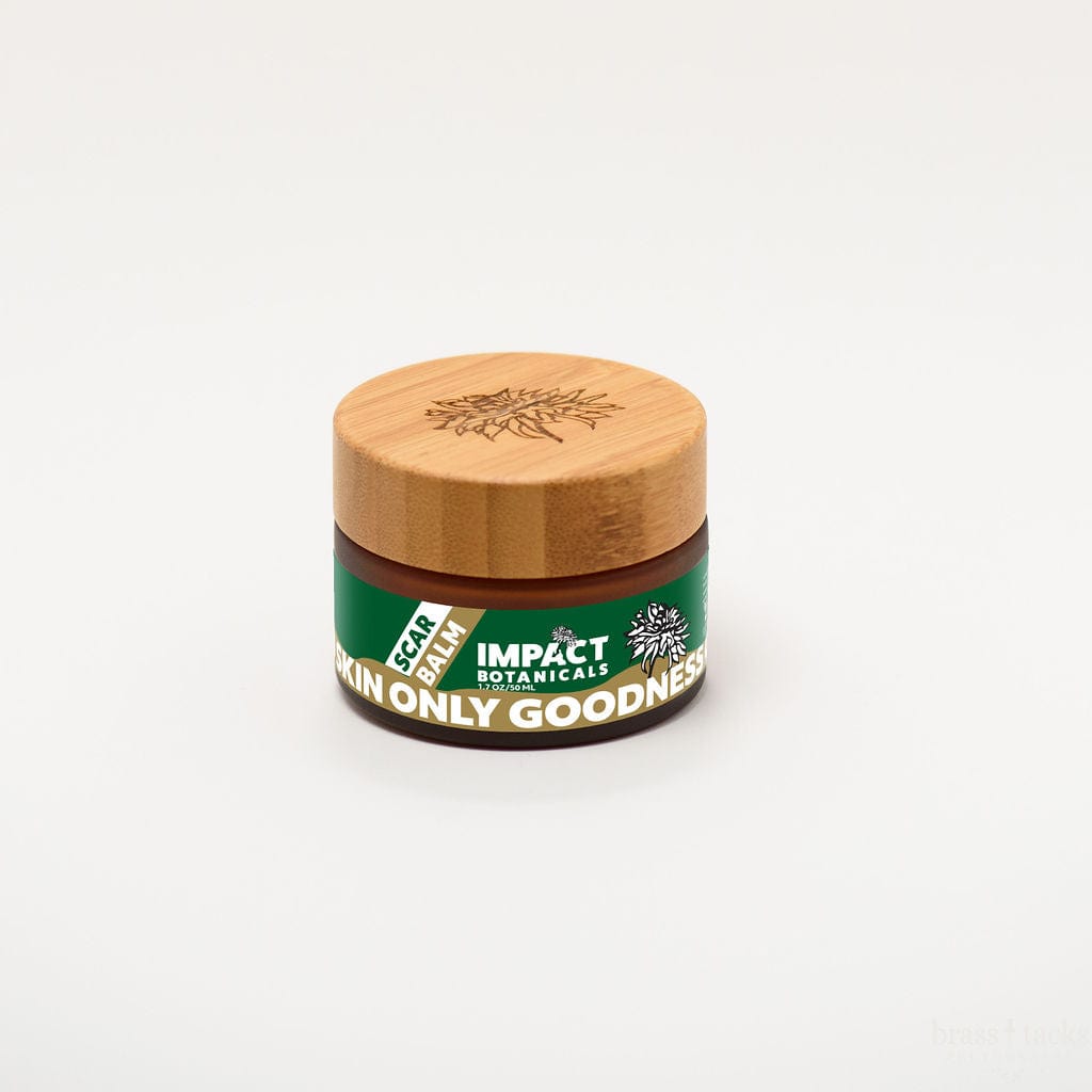 An amber jar of Impact Botanicals Scar Balm sits on a white background. The jar features a bamboo lid and green label that reads "Skin Only Goodness."