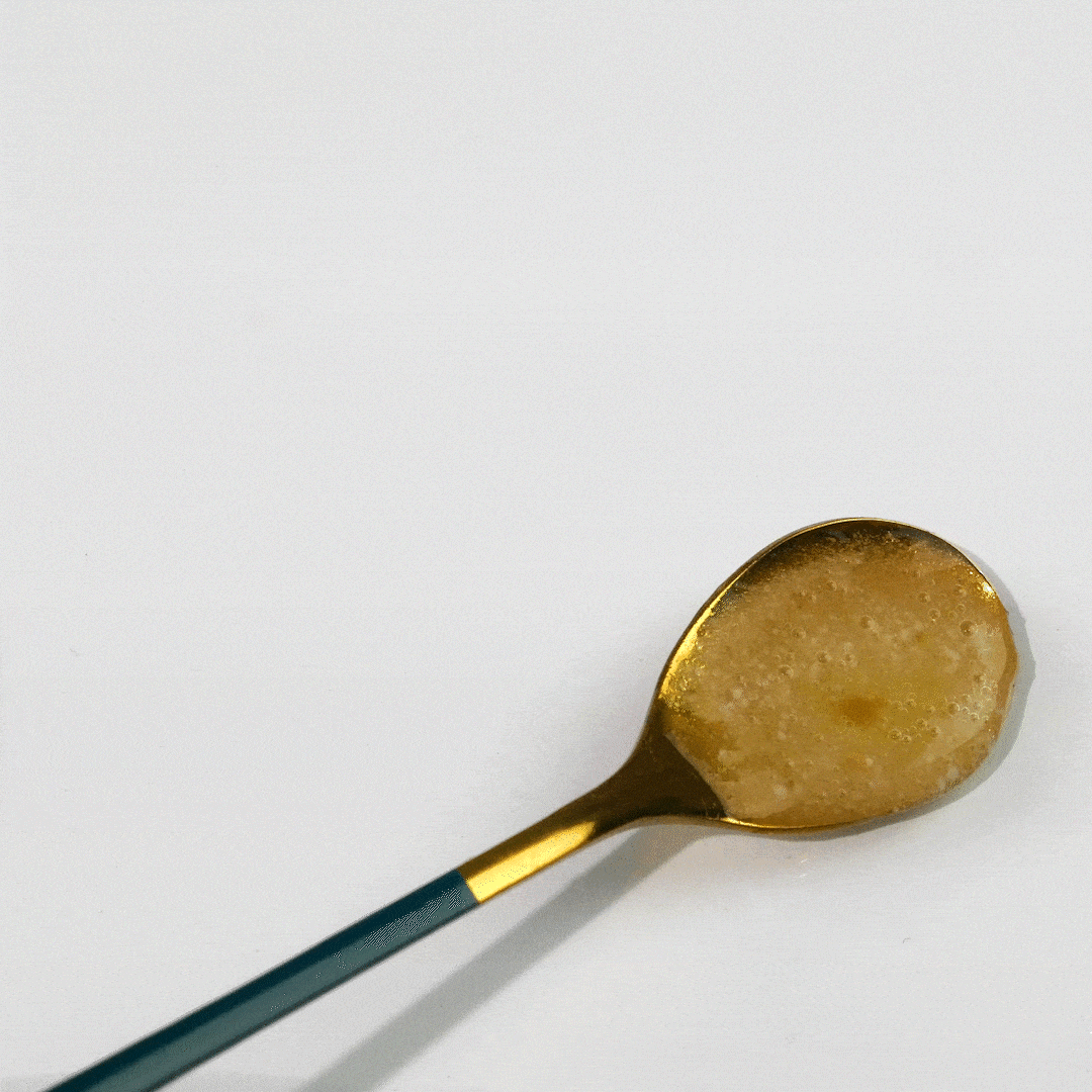 A gold spoon with a teal blue handle holds a spoonful of raw, unfiltered honey.