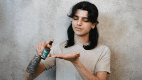 Man sprays beard oil onto open palm for beard grooming routine.