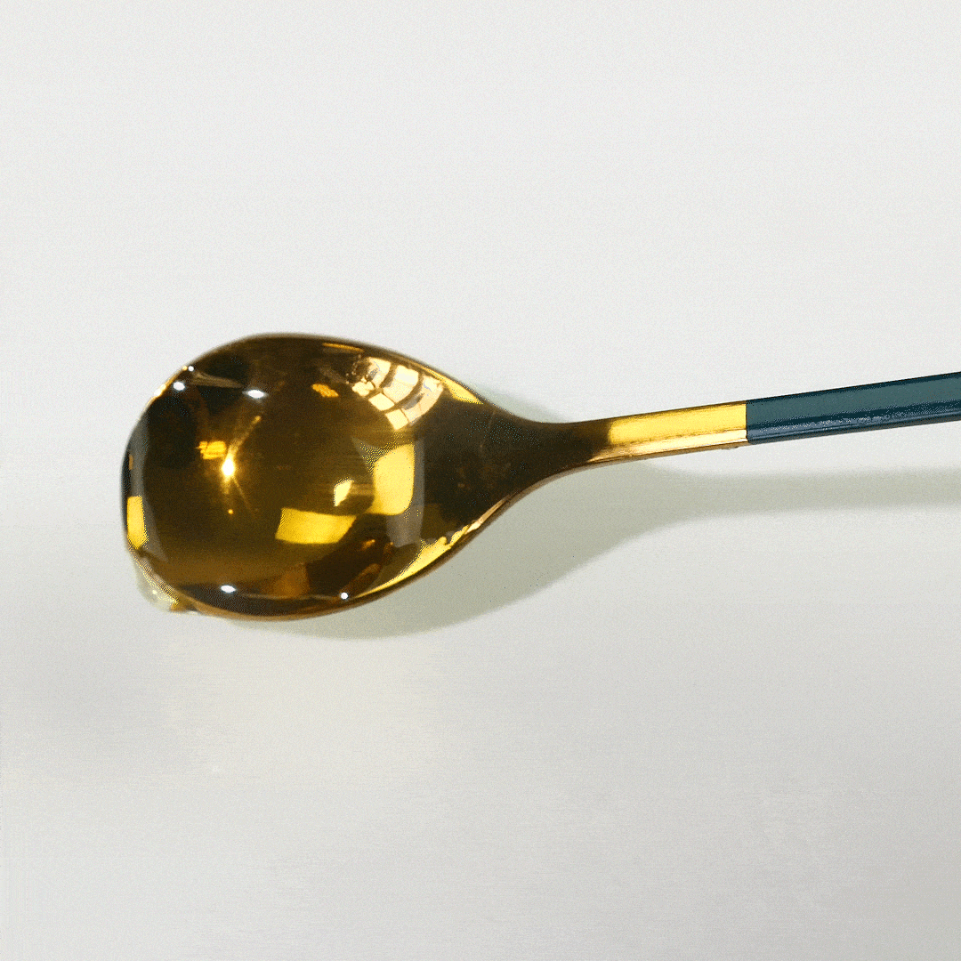 Gold spoon holds shimmering honey against a white background.