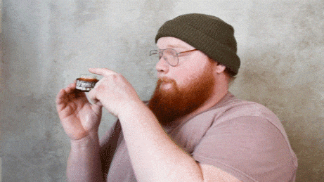 "Man examines a small jar of beard balm."