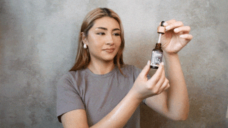 Woman dispenses serum from a brown glass dropper bottle.