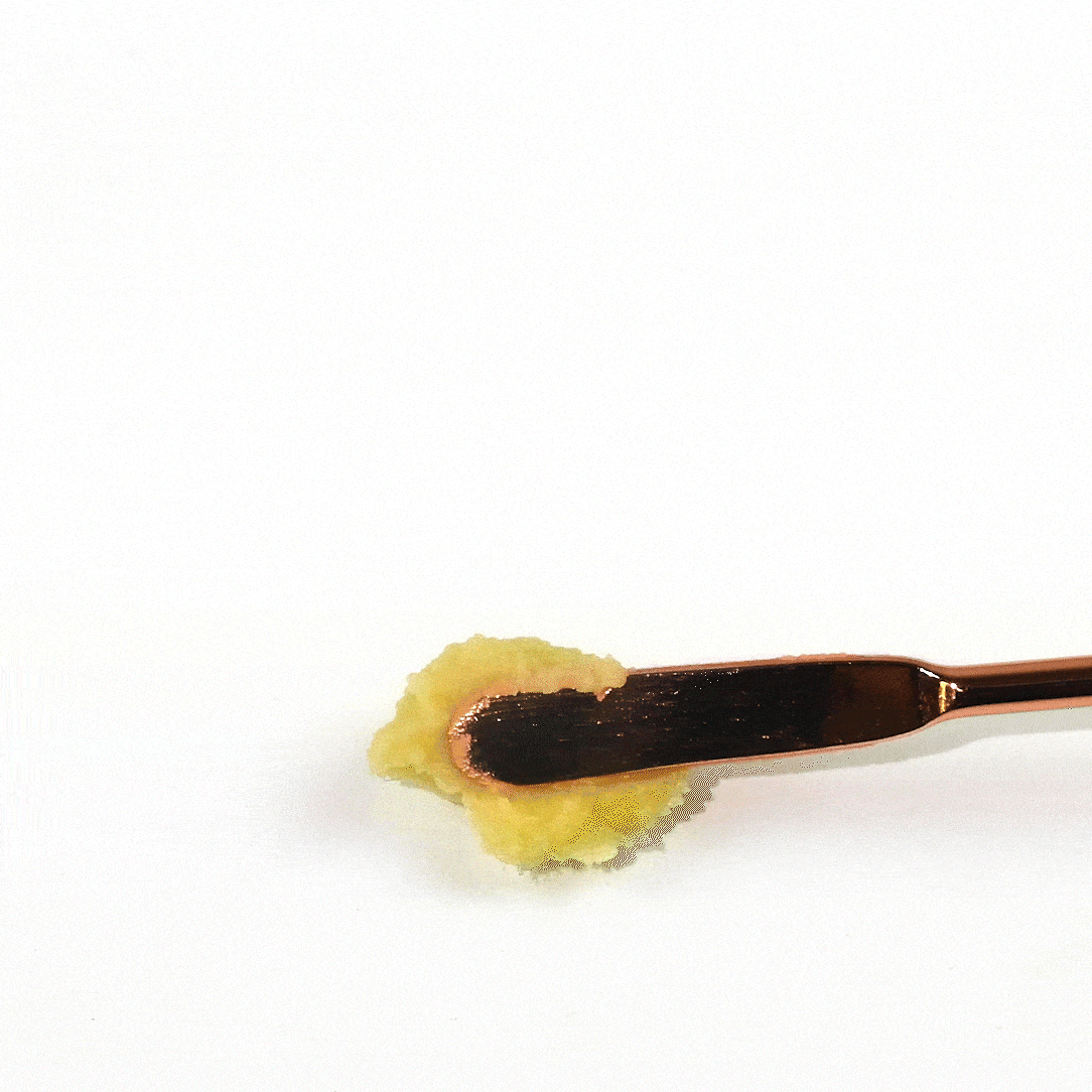 Rose gold makeup spatula scoops bright yellow facial cream.