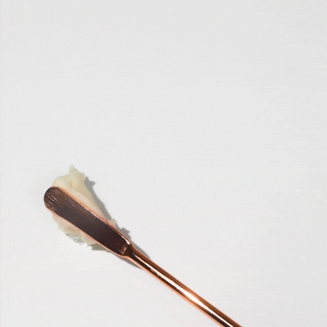 Rose gold applicator scoops thick white cream from jar.