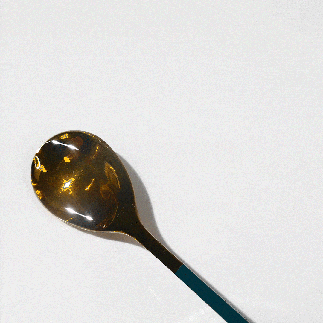 Gold spoon with teal handle casts a shadow on a white surface.